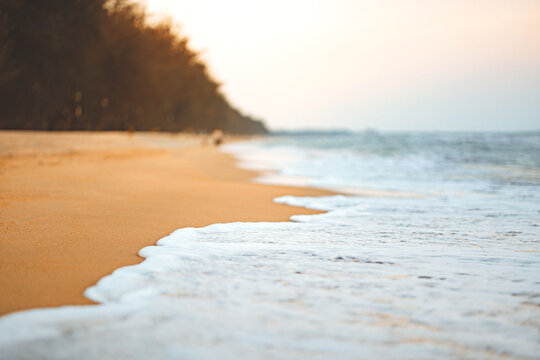 Close up of soft sea wave rolling onto sandy beach under bright sunlight, beautiful tropical seashore background for summer holiday vacation, wellness retreat, travel tourism, and peaceful nature