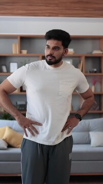 A young man of Indian and Arab descent performs a side bend stretch in his modern living room, focusing on core strength and flexibility