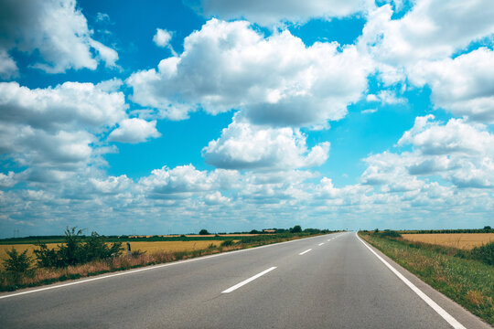 Open country road under blue sky with puffy clouds stretching to the distant horizon