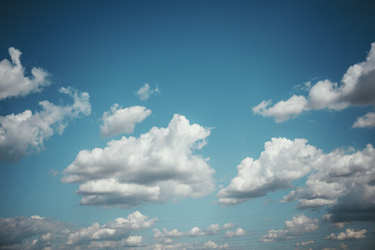 Soft, sunlit cumulus clouds drift across a clear blue sky, creating a calm, airy cloudscape ideal for backgrounds, weather concepts and travel visuals