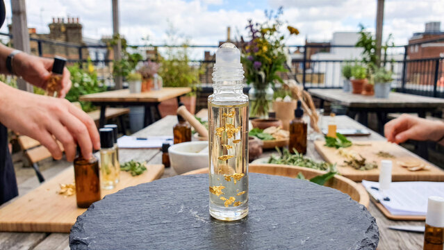 Clear glass roller bottle with transparent wellness oil and gold flakes at rooftop aromatherapy workshop