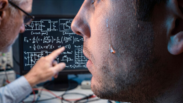 Extreme macro of young male coder cheek with older mentor pointing complex math schematic behind
