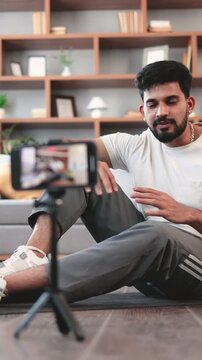 A young Indian man records himself giving fitness advice on his smartphone, surrounded by workout gear in a home setting