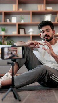A multiracial man records a workout video on his smartphone, demonstrating an exercise with dumbbells and a water bottle nearby