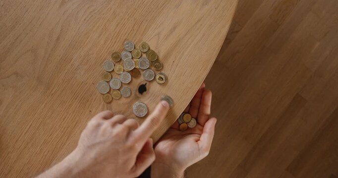 Top view of a person counting coins on a wooden table. Financial concept of budgeting, savings, expenses, personal finance, and money management.