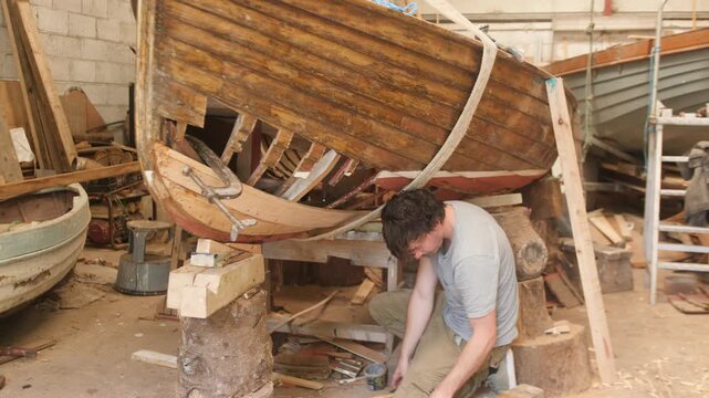 Young man fastening hull planks of clinker wood boat