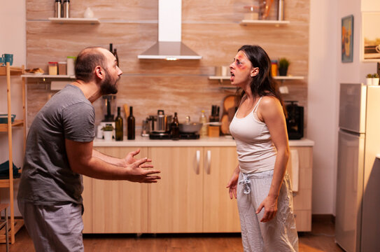 Drunk partner abuses and fights with his wife in the kitchen, showing fear, bruises, aggression and domestic violence inside a tense home conflict.
