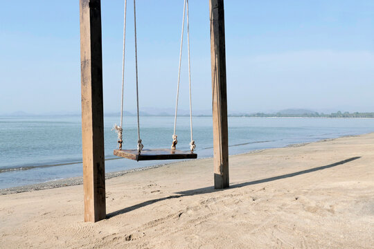 A wooden hanging swing on the beach by the sea.