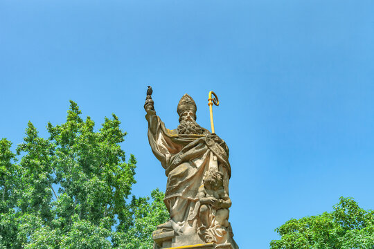 Antique statue of st. Augustine of Hippo and gray crow on Charles Bridge in Prague, Czech Republic