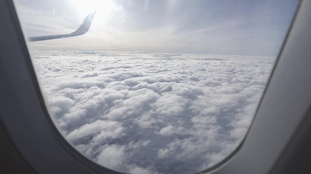Aerial view through plane window with view of clouds and plane wing in sky inspiration concept cinematic breathtaking aerial flying over white fluffy cloudscape in high altitude sky with clean sky