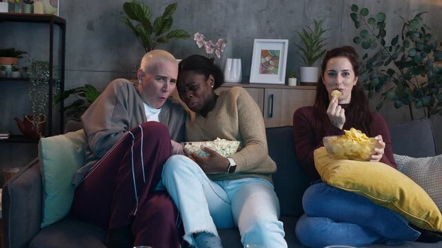 Diverse female friends watching scary movie together on sofa