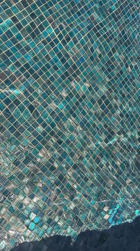 Clear blue water with gentle ripples over turquoise mosaic tiles in a swimming pool