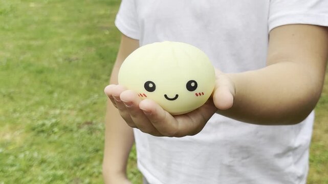 Person holding a cute smiley toy outdoors squishy Rainbow Mystery Bun 