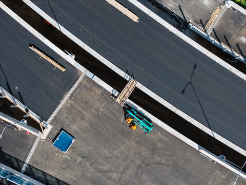 Aerial view of a new road construction site with workers in orange high-visibility vests and heavy machinery on the asphalt surface in Riga, Latvia.