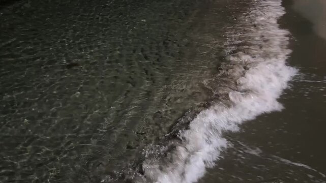 Dark sea water surface at night with illuminated texture and ripples near the shore