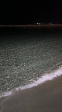 Dark sea water surface at night with gentle ripples and distant city lights on the horizon