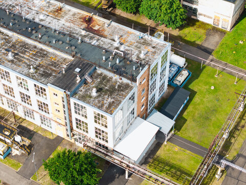 Aerial view of an industrial factory building with a flat roof, large windows, and surrounding green space in Olaine, Olaine Municipality, Latvia.