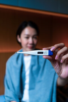 Close-up of a thermometer displaying body heat, held by Asian female patient. Concept of medical checkup, normal temperature, illness prevention, and daily self-care. Vertical Shot