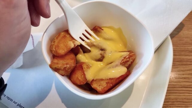 Potatoes grill&eacute;es recouverte de fromage fondu (cheddar), dans un petit bol blanc. Une fourchette est plant&eacute; dans le plat.