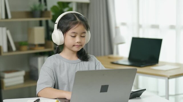 Young girl wearing large headphones and concentrating on laptop in a cozy home setting, creating an educational or entertainment environment