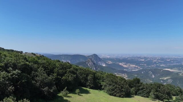 Vista da un drone che sorvola la cima della montagna, scivolando lungo il pendio verso la linea degli alberi e aprendo la vista su un&rsquo;ampia valle con montagne rocciose e paesaggi naturali