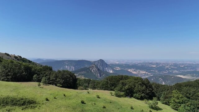 Vista da un drone che sorvola la cima della montagna, scivolando lungo il pendio verso la linea degli alberi e aprendo la vista su un&rsquo;ampia valle con montagne rocciose e paesaggi naturali