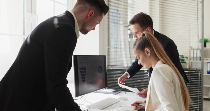 Team coworkers meeting for analysis and planning. In a bright office two men and a woman review computer charts and paperwork to guide business. Concept office teamwork and financial planning.