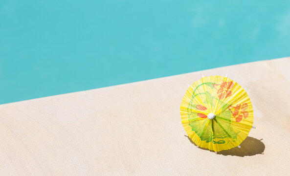 Yellow paper umbrella on swimming pool edge, summer season background