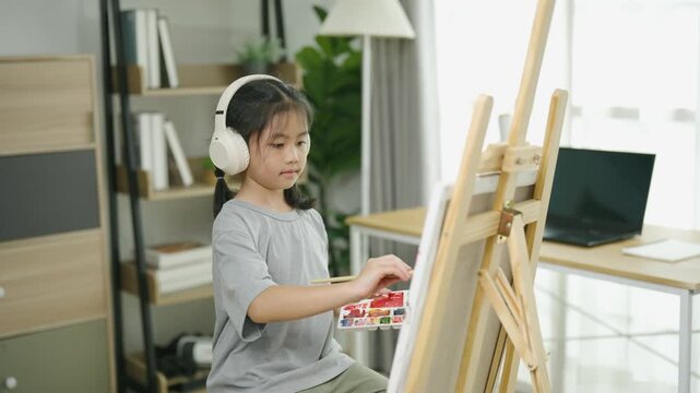 Young girl painting on canvas with art supplies in a cozy home workspace with shelves, plants, and a computer to inspire creativity and learning