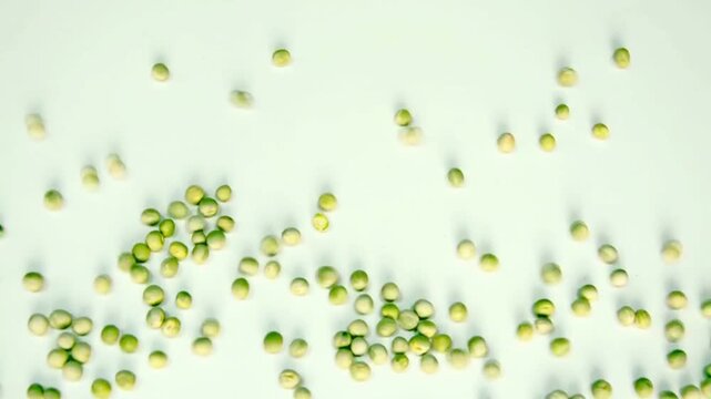 Overhead view of organic green split peas scattering dynamically onto a bright white background