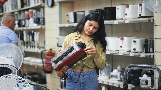 Latin woman stands in a store with appliances and chooses a toaster for her new modern kitchen. Woman looking at the assortment of toasters in the store. High quality 4k footage