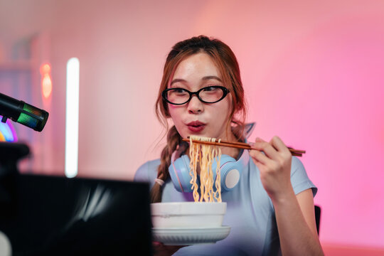 Young woman streamer glasses headphones eating instant noodles l