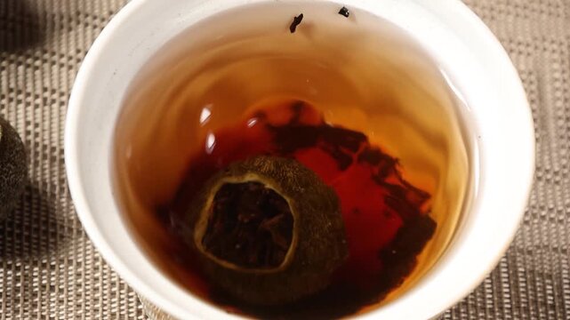 Slow motion close up of water droplet dripping into brewed mandarin puer tea