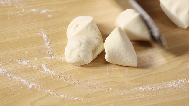 Close-up of cutting dough with a knife on a wooden cutting board sprinkled with flour.