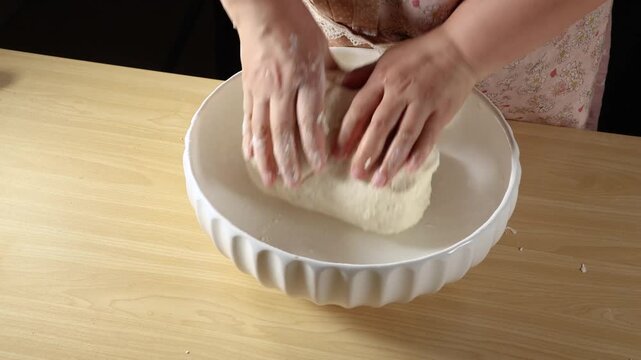 Close up of hands kneading dough in a white bowl on a wooden table