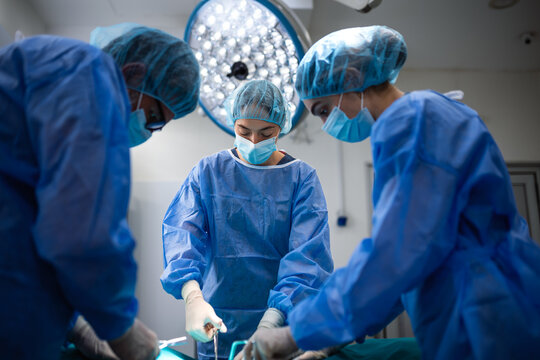 Focused female surgeon and medical team working together in a hospital operating room. Professional surgeons perform a successful operation in a sterile clinical environment using medical equipment.