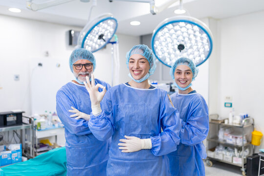 Team of surgeons and doctors standing in a hospital operating room after a successful operation. The female lead surgeon is smiling and gesturing an okay sign, showing confidence in medical care.