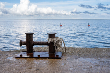 Rusty mooring bollard with a weathered rope on a concrete pier overlooking a calm sea under...