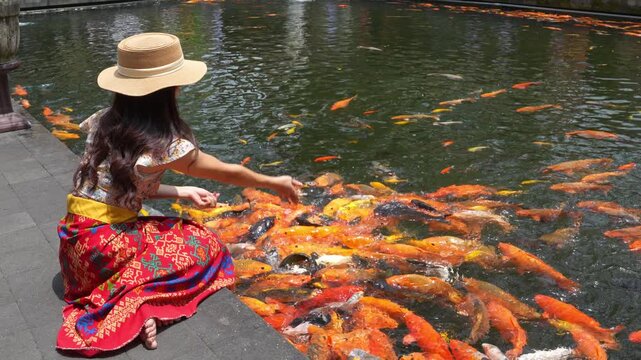 Female tourists feed fish at Tirta Empul, Bali&rsquo;s sacred water temple, reflecting Indonesia&rsquo;s spiritual heritage, cultural tourism, and peaceful temple atmosphere with holy spring waters.