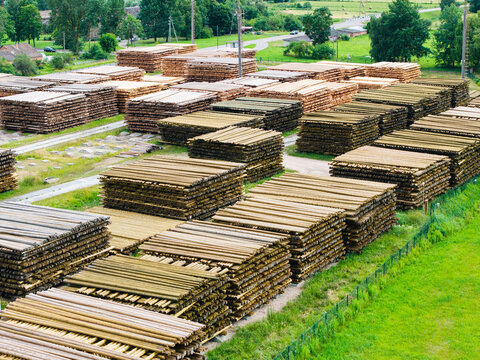 Aerial view of stacked logs in a timber yard, showcasing sustainable forestry practices with rows of cut wood and green fields in the background in Latvia.