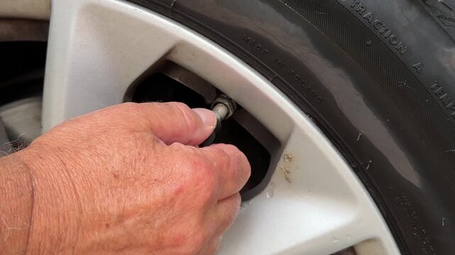 Close up of man hands connecting air compressor pump hose nozzle to car tire valve.