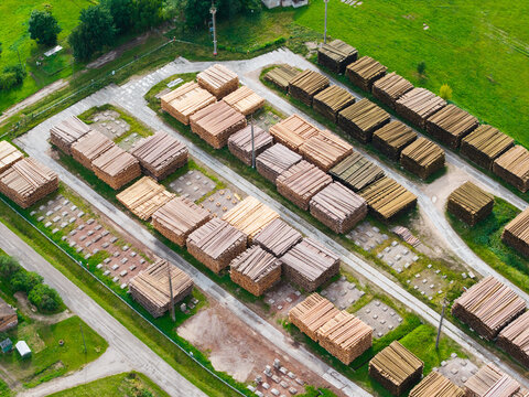 Aerial view of a large timber yard with neatly stacked lumber and logs arranged in rows across a green industrial site in Latvia.