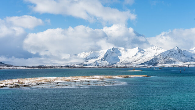 Landscape in the Vesteralen islands in Norway with snow covered mountains and blue sky, seen from the water