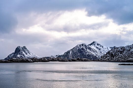 Landscape in the Lofoten islands in Norway with snow covered mountains and blue sky, seen from the water