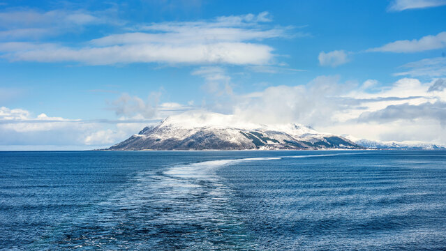 Landscape in the Vesteralen islands in Norway with snow covered mountains and blue sky, seen from the water