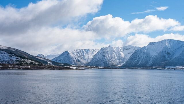 Landscape in the Vesteralen islands in Norway with snow covered mountains and blue sky, seen from the water