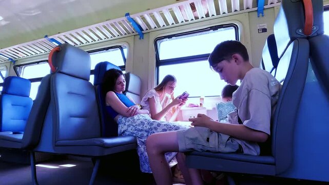 A mother with her children sitting inside a passenger train car and using smartphones while traveling during a summer journey. High quality 4k footage