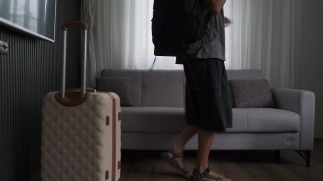 Rebuilding life in temporary housing. Man arriving at rented apartment with luggage and backpack, looking around and adjusting to a new environment