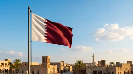National flag of Qatar waving on pole against traditional Arabic city architecture and blue sky © ZiletterId