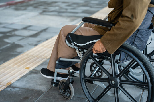 A man with a leg disability who cannot walk uses a wheelchair and travels by the train at a station He walks along the sidewalk where there are signs indicating accessibility for disabled individuals